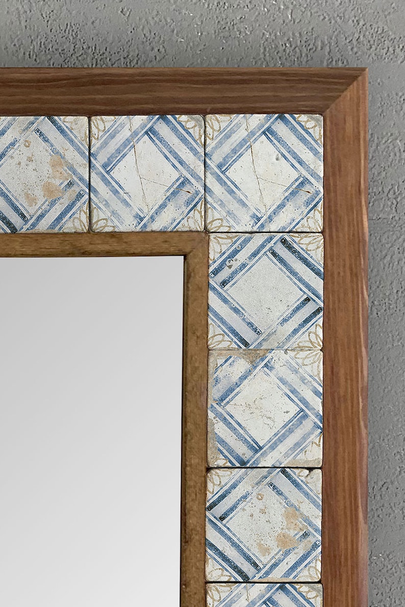 May include: A rectangular mirror with a wooden frame. The frame is decorated with square tiles featuring a blue and white geometric pattern. The mirror is a decorative item.