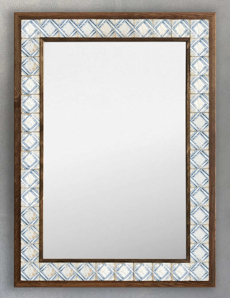 May include: Rectangular mirror with a dark brown wooden frame. The frame is accented with a border of square tiles in white and blue geometric patterns. The mirror's reflective surface is clear.