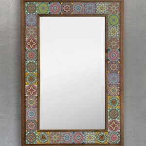 Op de afbeelding: Rechthoekige wandspiegel met een houten frame. Het frame is versierd met kleurrijke, patroon tegels in tinten blauw, geel, rood en groen. Het reflecterende oppervlak van de spiegel is helder en het ontwerp is decoratief.