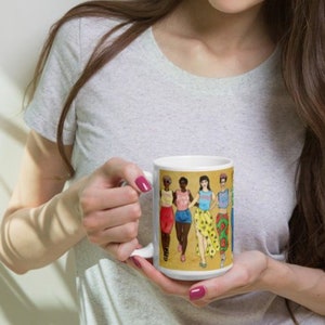 May include: White ceramic mug with a colorful illustration of five women wearing different outfits. The women are standing in a line and smiling. The mug is being held by a person.