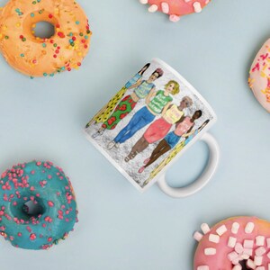 May include: White ceramic mug with a colorful illustration of six women standing together. The women are wearing different outfits and have different hairstyles. The text on the mug reads "Girls Just Wanna Have Fun".