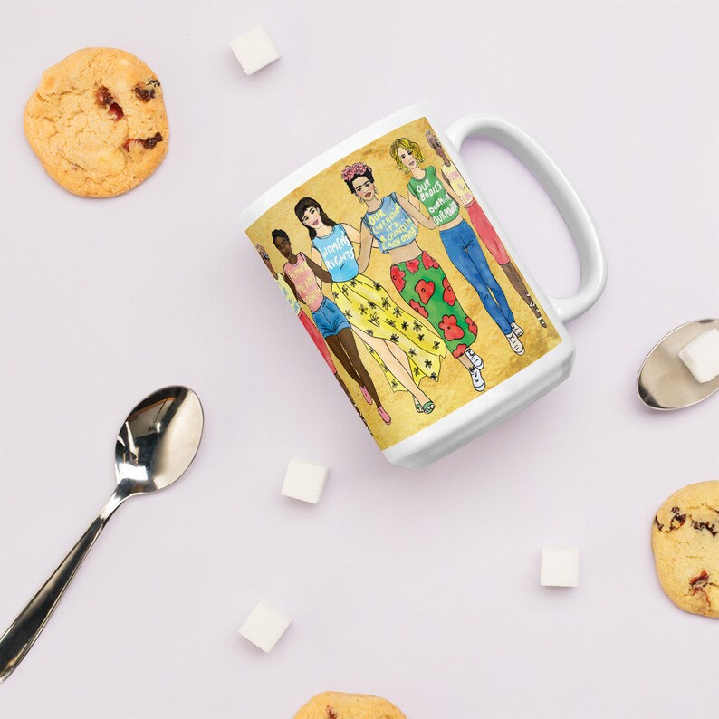 May include: White ceramic mug with a colorful illustration of six women holding hands. The women are wearing different outfits and have different hairstyles. The text on the mug reads "Our Bodies Our Rights Our Choices Our Future".