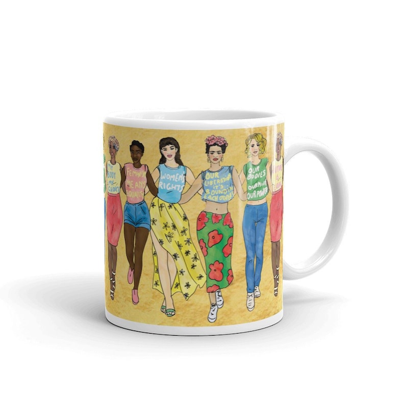May include: White ceramic mug with a colorful illustration of six women holding hands. The women are wearing different outfits and have different hairstyles. The mug has the text "My Body My Choice", "Feminist AF", "Women's Rights", "Our Liberation Is Bound In Each Other", "Our Bodies Our Power", and "Our Power" on it.