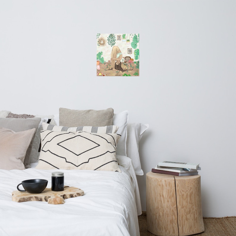 Puede incluir: Una impresi&oacute;n art&iacute;stica enmarcada que presenta una ilustraci&oacute;n de una persona cuidando plantas. La obra de arte tiene una paleta de colores neutros con follaje verde y un fondo marr&oacute;n claro. La impresi&oacute;n se muestra en una pared blanca sobre una cama.