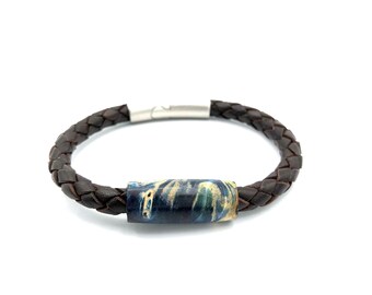 May include: A brown leather bracelet with a braided design and a blue and green patterned wooden bead.