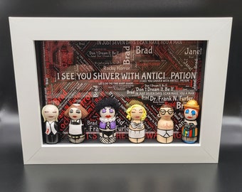 May include: A framed set of 7 hand-painted wooden figures, each depicting a character from the musical "Rocky Horror Picture Show". The figures are arranged in a row, with the text "I SEE YOU SHIVER WITH ANTICI...PATION" printed on the background.