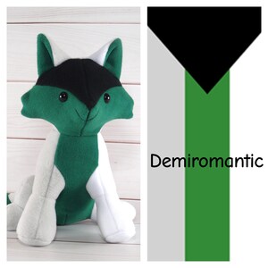 May include: Green and white plush toy shaped like a fox with black ears and a black nose. The toy is sitting on a white wooden surface. The text "Demiroamtic" is written in black on a white and green background.