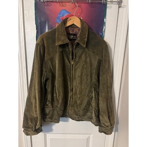 May include: An olive green corduroy jacket featuring a full-length front zip, a pointed collar, and long sleeves with cuffed wrists. The interior lining displays a multicoloured paisley pattern, and a black label reads Oakbrook Sportswear.