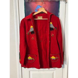 May include: A vintage red jacket with embroidered details. The jacket features a collared neckline, two front pockets, and decorative stitching along the edges. The embroidery includes yellow, gray, and green elements, depicting houses and figures.