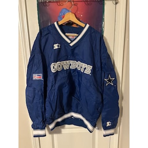 Puede incluir: Chaqueta cortavientos azul Starter con detalles blancos y grises. La palabra "COWBOYS" está en letras blancas en el pecho. Una estrella blanca está en la manga derecha. La chaqueta tiene cuello en V y una franja blanca en la parte inferior.