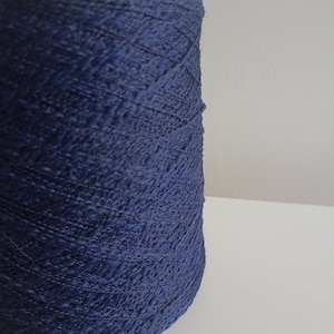 May include: A large cylindrical spool of deep navy blue yarn. The yarn features a textured, slightly irregular ply with a matte finish, wound tightly in a consistent pattern around the central core, showcasing the rich, dark blue colour throughout.
