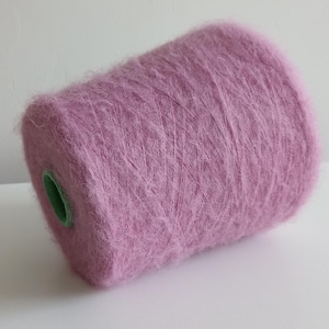 May include: A lilac-coloured yarn spool. The yarn is fluffy and appears to be made of a delicate fibre. The spool has a green core. Suitable for knitting, crochet, and other fibre art projects.