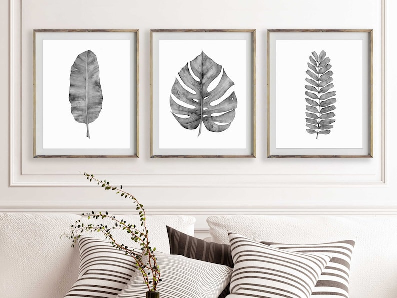 Puede incluir: Tres impresiones enmarcadas en blanco y negro de acuarela de hojas tropicales. Las impresiones est&aacute;n en marcos plateados simples y est&aacute;n colgadas en una pared blanca.