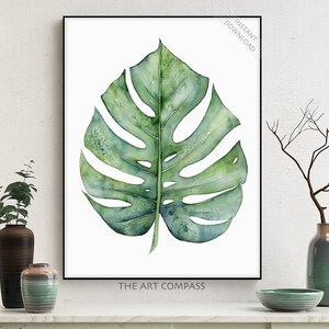 May include: A watercolor painting of a large, green monstera leaf. The leaf is depicted in a realistic style with intricate details and subtle shading. The painting is framed and displayed on a white background.