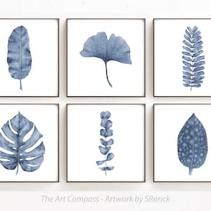 May include: Set of six blue watercolor prints featuring various leaf designs. The prints are framed in black and arranged in a grid pattern on a white wall. The Art Compass - Artwork by SRorick is printed at the bottom of the image.