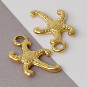 May include: Two gold-tone metal starfish charms with a loop for attaching to jewelry or other crafts. The charms have a detailed design and a textured surface.