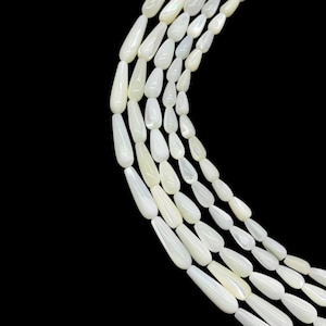 May include: A collection of white, teardrop-shaped beads arranged in a curved, multi-strand pattern against a black background. Each bead features a smooth, polished surface with a subtle iridescent sheen, reflecting light along its length.