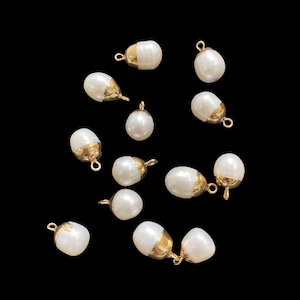 May include: A selection of white, teardrop-shaped pearl beads with gold-coloured caps and loops. The beads are scattered against a black background, highlighting their lustre and design. Suitable for jewellery making.