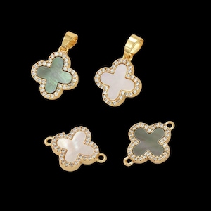 May include: Four gold-coloured clover pendants with white and grey-green centres. Each clover is outlined with small, clear crystals. Two pendants have a loop at the top, and two have loops on the sides for jewellery making.