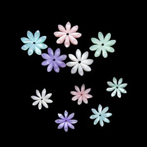 May include: A collection of ten flower-shaped embellishments in various pastel colors, including light blue, pink, purple, white, and green. The petals are translucent, and the background is black.