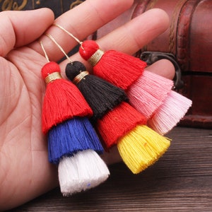 May include: Five multi-coloured tassel trims with gold accents. The tassels are layered in red, blue, white, yellow, pink, and black.