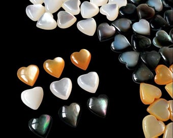 May include: An assortment of heart-shaped beads in various colors, including white, gold, black, and iridescent hues. The beads are scattered against a black background, creating a visually appealing contrast. These beads are suitable for jewelry making and craft projects.