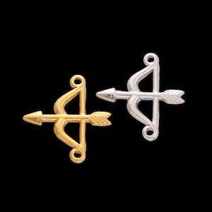 Peut inclure: Deux pendentifs en forme d'arc et de flèche, l'un doré et l'autre argenté, sur fond noir. Les pendentifs présentent un arc courbé et une flèche droite, avec un design minimaliste, pour bijoux.