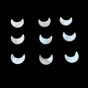 Può includere: Nove pezzi a forma di mezzaluna con finitura perlescente e iridescente. I pezzi sono disposti in una griglia di tre per tre su uno sfondo nero pieno. Le forme di luna hanno un design liscio e curvo.