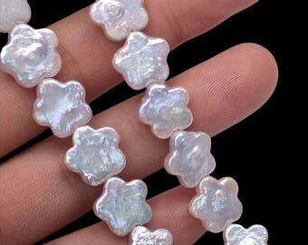 Peut inclure: Gros plan sur un fil de perles blanches en forme de fleurs. Les perles ont un éclat nacré irisé, avec de subtiles nuances de rose et de bleu. Les pétales de chaque perle sont clairement définis, créant une apparence délicate et élégante. Le fond est noir.