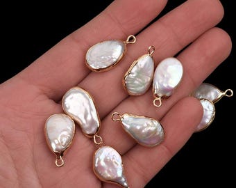 May include: A collection of irregularly shaped, white freshwater pearls with a gold-colored metal trim and loop. The pearls have a lustrous, iridescent sheen. The pearls are displayed against a dark background.