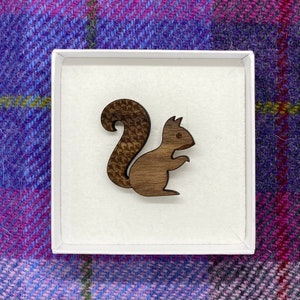 May include: A wooden squirrel brooch in a white box. The squirrel is brown and has a detailed tail.