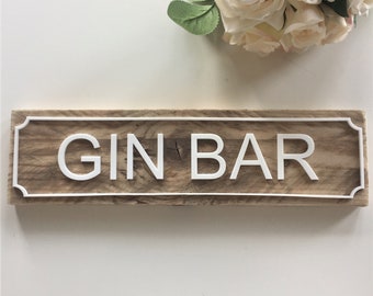 May include: A wooden sign with a white border and the words "GIN BAR" in white raised letters.