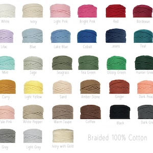 Op de afbeelding: Een collectie van eenendertig klossen gevlochten 100% katoenen koord gerangschikt in een raster, elk gelabeld met de specifieke kleurnaam, waaronder wit, ivoor, roze, rood, blauw, groen, geel, bruin, grijs en zwart.