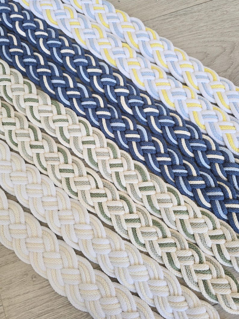 Op de afbeelding: Vijf parallelle stroken gevlochten stof, diagonaal gerangschikt. De kleurcombinaties omvatten wit met geel, donkerblauw met lichtblauw, saliegroen met cr&egrave;me, lichtgeel met cr&egrave;me en een effen cr&egrave;mekleurig gevlochten koordontwerp.
