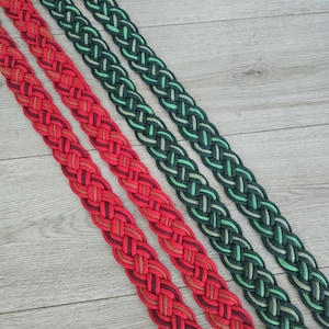 Op de afbeelding: Twee lange, platte, gevlochten textielbanden die diagonaal zijn gerangschikt. De ene band heeft een verloop van rode, oranje en diepe bordeauxrode tinten, terwijl de andere band een verloop van donker bosgroen, smaragd en licht limoengroen toont.