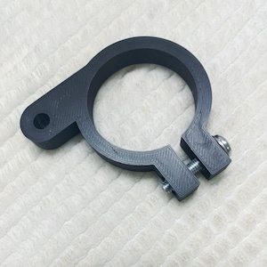 May include: A black plastic clamp with a screw and a round opening. The clamp is designed to hold a pipe or other round object.
