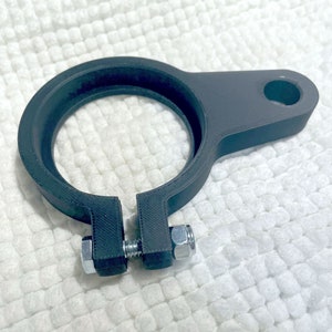 May include: A black plastic clamp with a round opening and a side arm. The clamp has two silver screws.