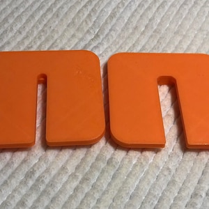 May include: Two orange plastic pieces shaped like the letter "n" with a cut-out in the middle.