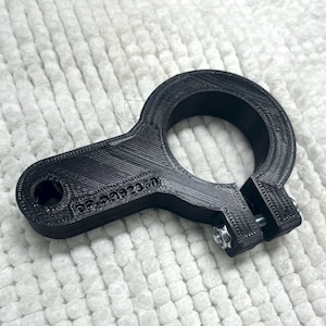 May include: Black plastic clamp with a round opening and a screw on the side. The clamp has the text "DE-589233" printed on it.