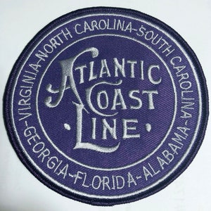 Peut inclure: Un écusson brodé violet avec le texte "Atlantic Coast Line" en écriture cursive argentée. L'écusson est entouré d'un cercle argenté avec le texte "Virginia-North Carolina-South Carolina-Georgia-Florida-Alabama" en écriture cursive argentée.
