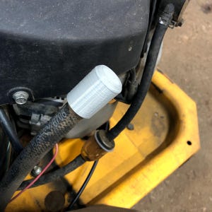 May include: Close-up of a gray plastic cap on a black hose with the text "ROUSH" and "48708". The hose is connected to a yellow engine.
