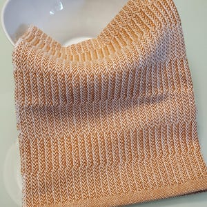 May include: A brown and white striped kitchen towel with a subtle herringbone pattern. The towel is folded and lying on a white surface.