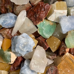 Puede incluir: Una colección de piedras preciosas naturales en bruto de varios colores, incluidos azul, verde, amarillo y rojo. Las piedras son de diferentes tamaños y formas, y algunas tienen una textura cristalina.