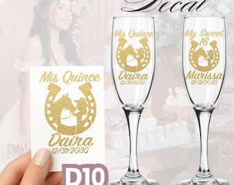 May include: Custom vinyl decals for champagne flutes. The decals feature gold text and a horseshoe design with the words "Mis Quince" and "My Sweet 16", along with names and dates. A white decal with the same design is also shown.