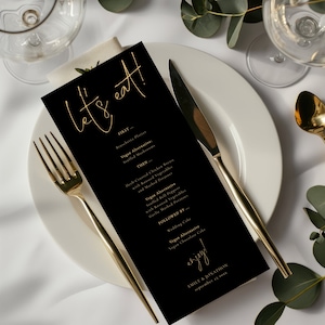 Puede incluir: Tarjeta de menú de boda negra y dorada con el texto "Let's eat!" en escritura dorada. El menú enumera las opciones de primer plato, plato principal y postre, incluidas alternativas veganas. La tarjeta también incluye los nombres de la pareja y la fecha de la boda.