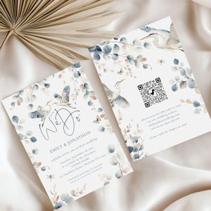 May include: A wedding invitation with a watercolor design featuring blue and white birds, eucalyptus leaves, and butterflies. The text on the invitation reads "We Do" and includes the names Emily & Jonathon, the date and time of the wedding, the venue name, and the address. A QR code is included on the invitation for guests to RSVP.