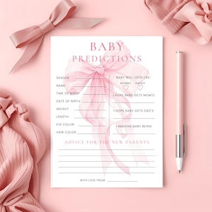 May include: A baby shower game card with the text "Baby Predictions" in pink. The card has spaces for details like gender, name, and eye color. A pink pen and decorative bow are also in the image.