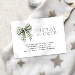 May include: A white card with green and white gingham bow and the text "DISPLAY SHOWER" in black. The card reads "Your thoughtful gift will be put on display So no need to wrap it in any way A ribbon or tie will do just great Leaving us more time to mingle and celebrate!"