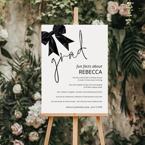 May include: A white sign with black text and a black bow on top. The sign says "fun facts about Rebecca" and lists some fun facts about Rebecca. The sign also says "Rebecca's graduation party. June 15 20XX".