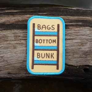 May include: A yellow and blue embroidered patch with a bunk bed and the text "Bags Bottom Bunk".